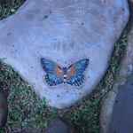Stepping stone dengan ornamen keramik motif kupu-kupu yang terletak di sudut.