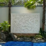 Batu alam ukir (batu candi) berwarna putih dengan motif bunga dan daun lotus. Batu ukir diletakkan di taman belakang.