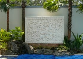 Batu alam ukir (batu candi) berwarna putih dengan motif bunga dan daun lotus. Batu ukir diletakkan di taman belakang.