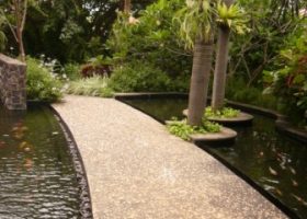 Jalur pejalan kaki menggunakan koral sikat tanpa motif berwarna terang di atas kolam.